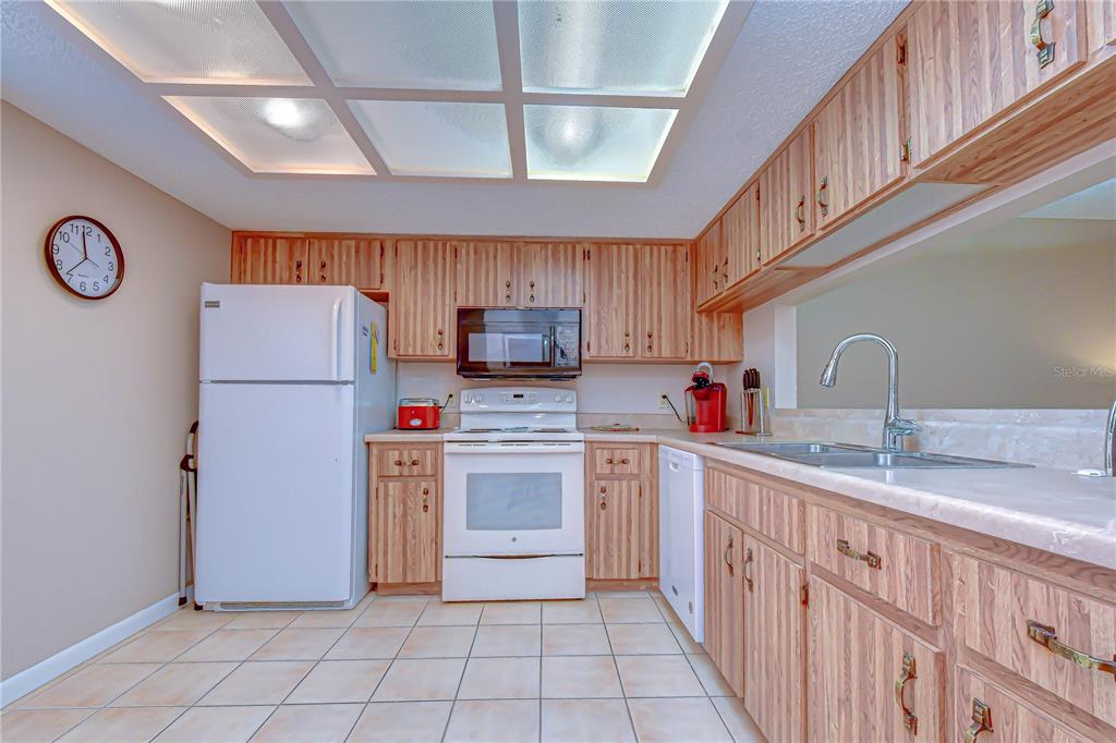 A kitchen features light wood cabinets, white appliances, tile flooring, and a drop ceiling — 38235 BOXWOOD DRIVE UNIT 38235, ZEPHYRHILLS, FL