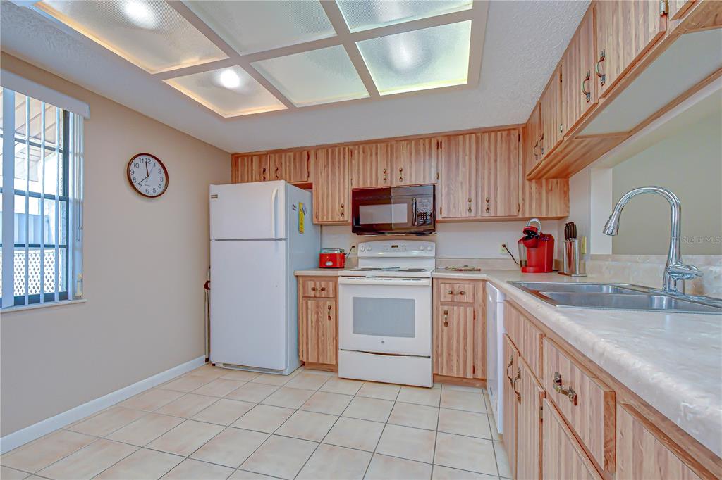 A kitchen with light wood cabinets, white appliances, tile flooring, and a drop ceiling — 38235 BOXWOOD DRIVE UNIT 38235, ZEPHYRHILLS, FL