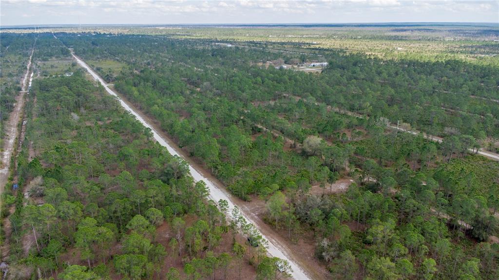 An aerial view shows a dirt road cutting through a flat, wooded landscape — 13 ALBA DRIVE, INDIAN LAKE ESTATES, FL