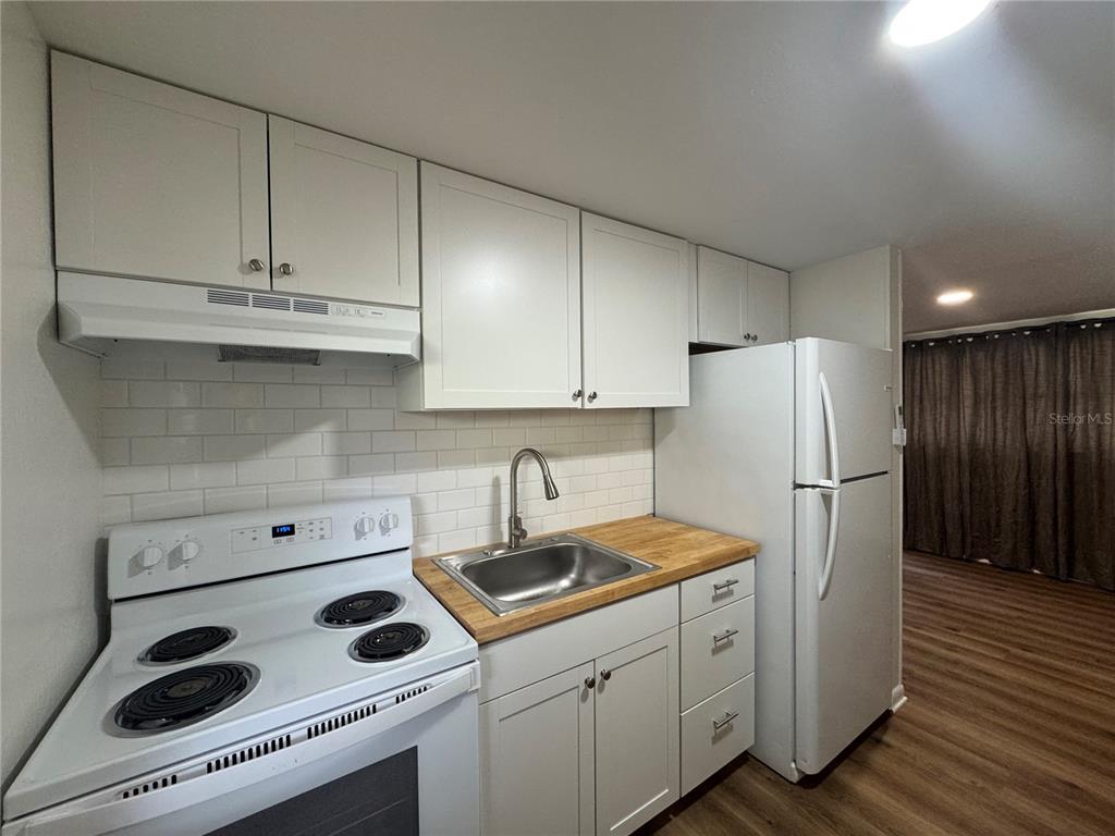 A kitchen features white cabinets, a butcher block countertop, a stainless steel sink, and appliances — 1801 N TAYLOR ROAD, BRANDON, FL