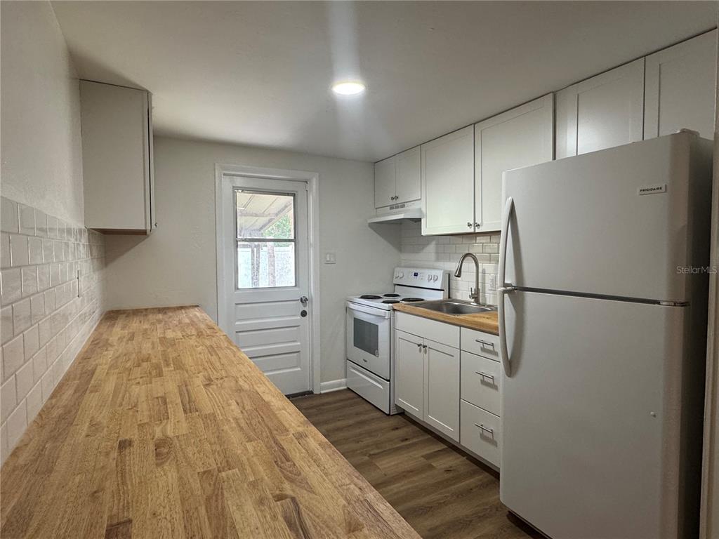 A galley kitchen features white cabinets, butcher block countertops, white appliances, and a back door — 1801 N TAYLOR ROAD, BRANDON, FL