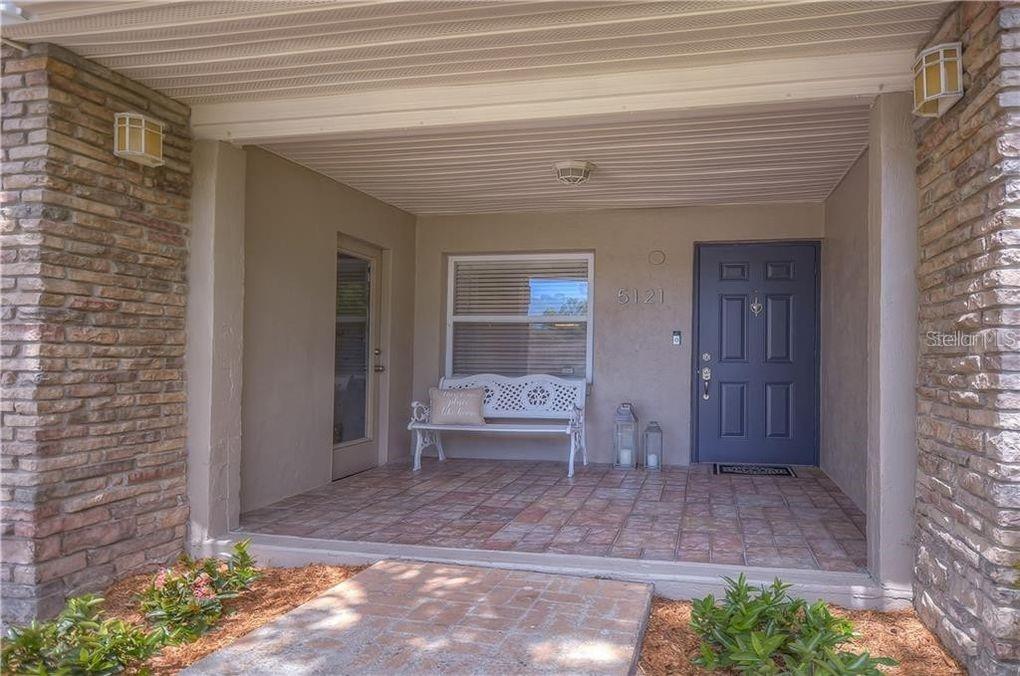 A covered front porch features a brick floor, a white bench, and a blue door — 5121 ELLENDALE AVENUE, TAMPA, FL