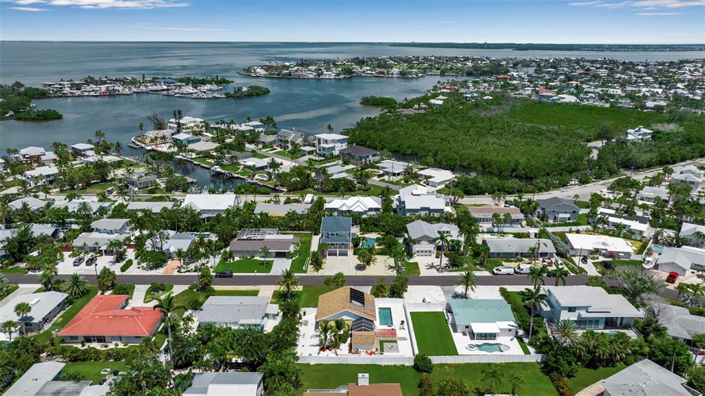 An aerial view shows a coastal neighborhood with houses, swimming pools, and surrounding waterways — 210 84TH STREET, BRADENTON BEACH, FL
