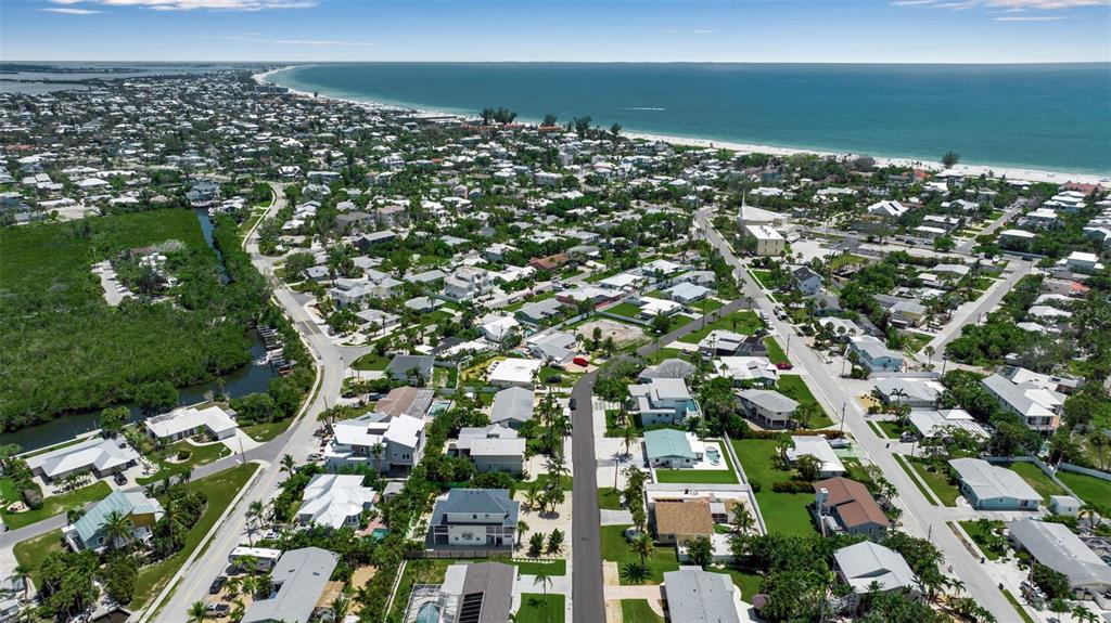 An aerial view shows a coastal neighborhood with houses, streets, and a nearby beach — 210 84TH STREET, BRADENTON BEACH, FL