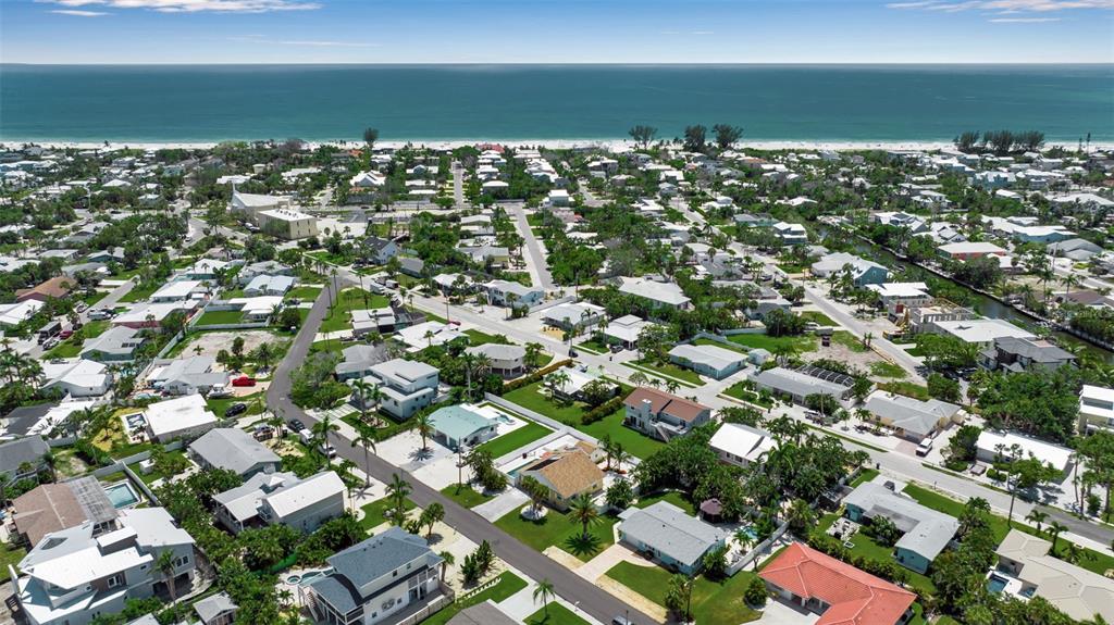 An aerial view shows a coastal neighborhood with houses, streets, and a beach in the distance — 210 84TH STREET, BRADENTON BEACH, FL