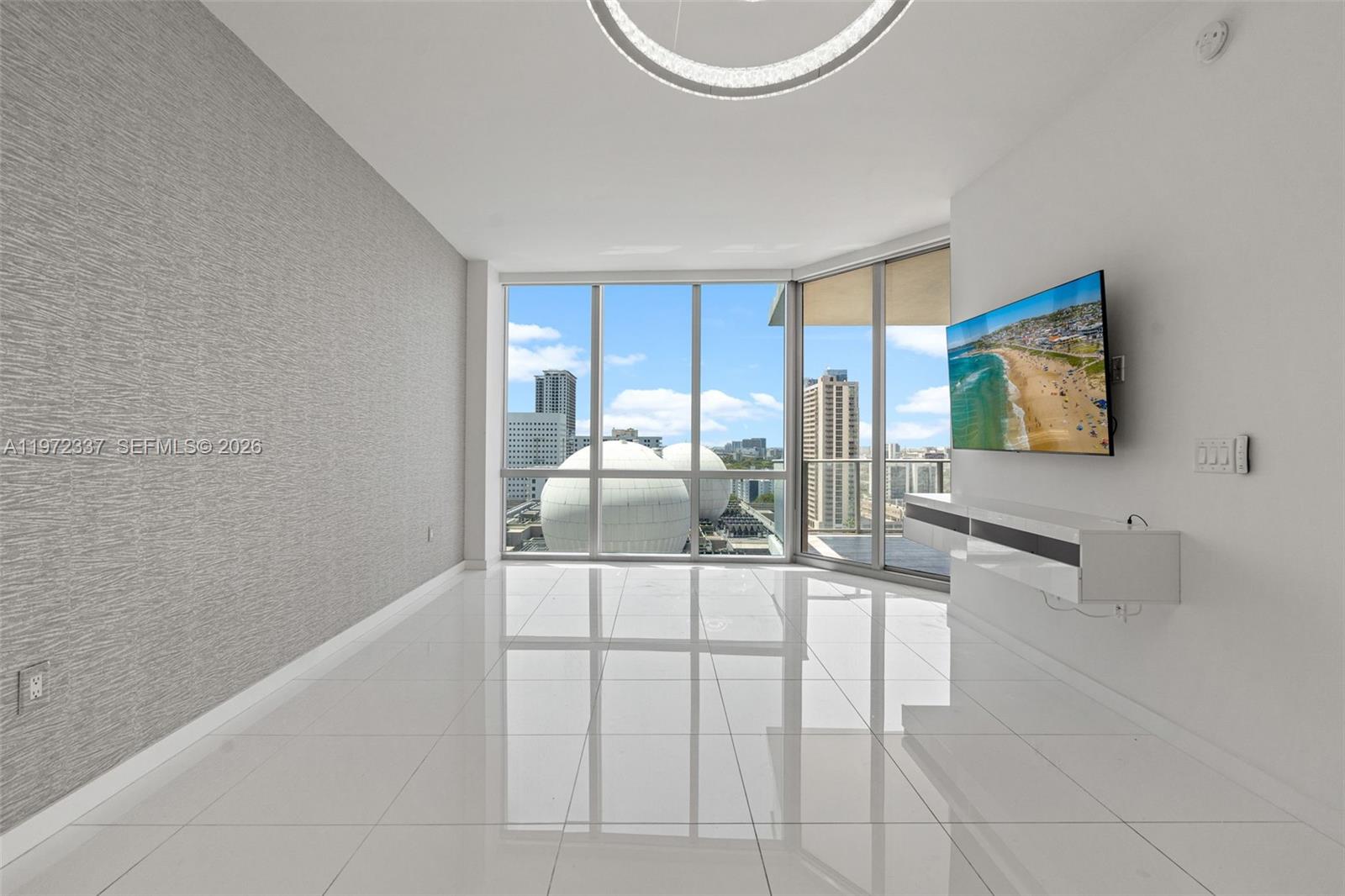 A modern living room features white tile floors, a textured gray wall, and floor-to-ceiling windows — 851 NE 1st Ave # 1506, Miami FL 33132, MIAMI, FL