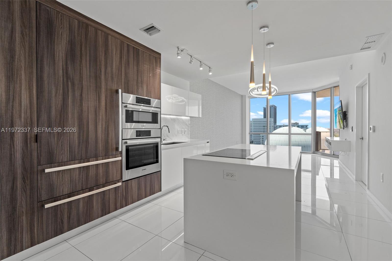 A modern kitchen features dark wood cabinetry, white countertops, an island, and floor-to-ceiling windows — 851 NE 1st Ave # 1506, Miami FL 33132, MIAMI, FL