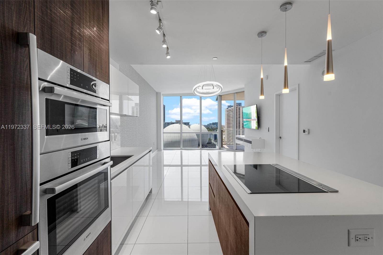 A modern kitchen features white cabinetry, a center island with a cooktop, and floor-to-ceiling windows — 851 NE 1st Ave # 1506, Miami FL 33132, MIAMI, FL