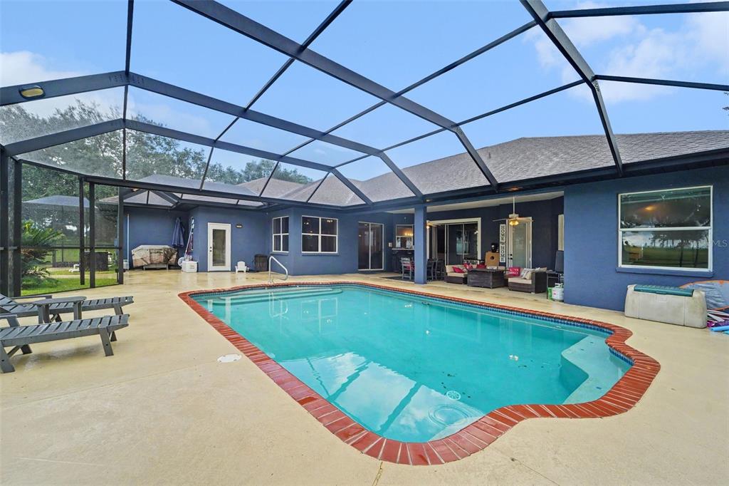 A screened-in swimming pool with a brick border sits on a concrete patio behind a house — 37616 SKY RIDGE CIRCLE, DADE CITY, FL