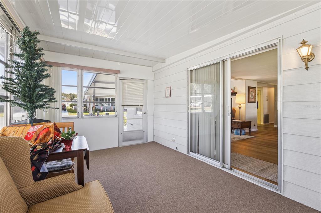 A sunroom with carpeted floors, a small Christmas tree, and sliding glass doors to the interior — 103 POINSETTIA, LEESBURG, FL