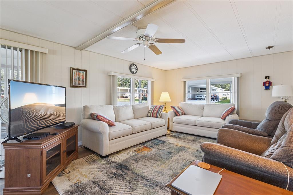 A living room features two beige sofas, two armchairs, a television, and a ceiling fan — 103 POINSETTIA, LEESBURG, FL