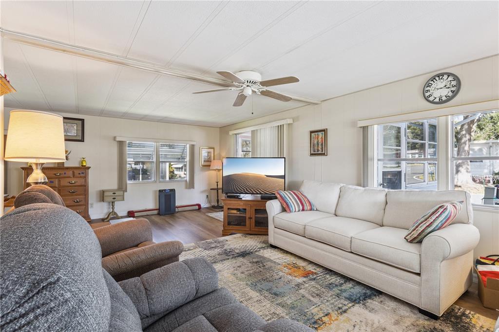 A living room features a white sofa, gray armchair, ceiling fan, and a wall clock — 103 POINSETTIA, LEESBURG, FL