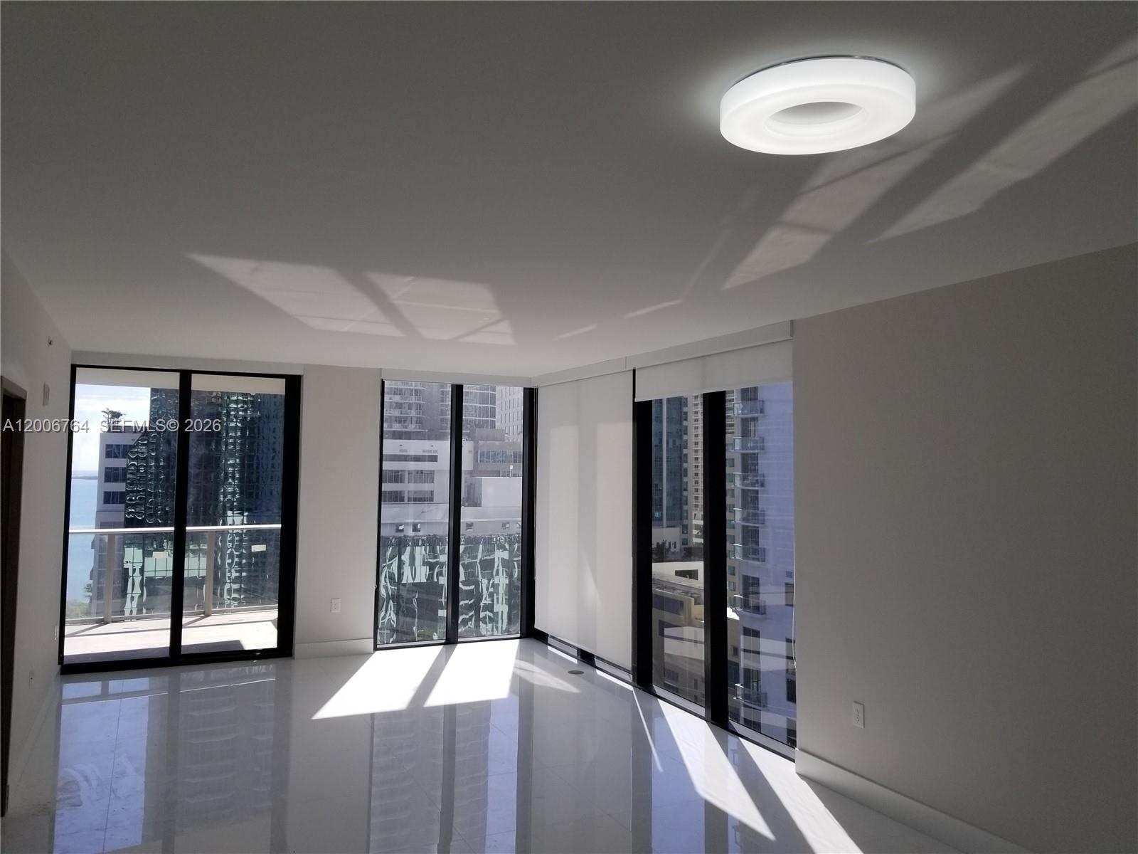 A bright, empty room features white tile floors, floor-to-ceiling windows, and a circular ceiling light — 1010 Brickell Ave # 3205, Miami FL 33131, MIAMI, FL