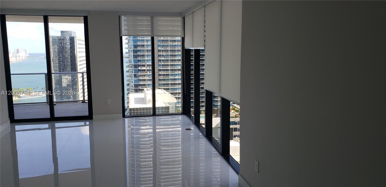 An empty room features white tile floors, floor-to-ceiling windows, and views of nearby skyscrapers — 1010 Brickell Ave # 3205, Miami FL 33131, MIAMI, FL