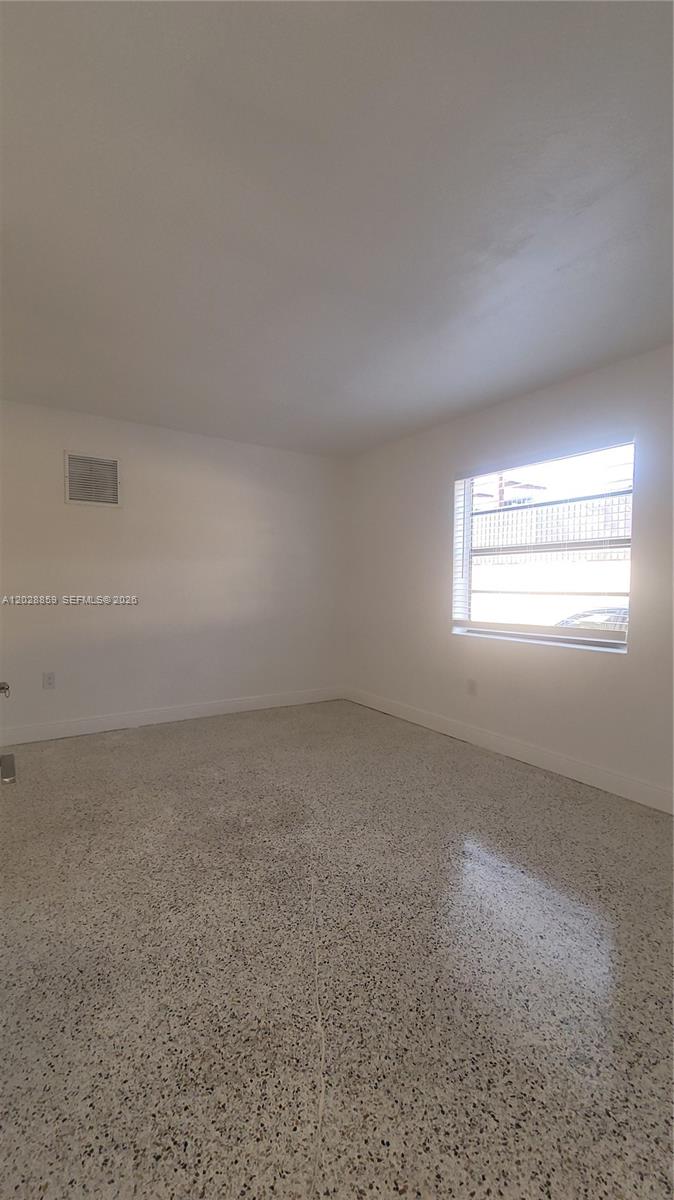 An empty room features white walls, a window with blinds, and speckled terrazzo flooring — 34 E 21st St # 3, Hialeah FL 33010, HIALEAH, FL