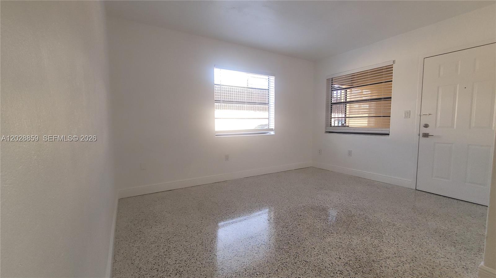 An empty room features white walls, two windows with blinds, and polished terrazzo flooring — 34 E 21st St # 3, Hialeah FL 33010, HIALEAH, FL