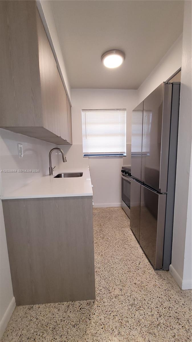 A galley kitchen features light wood cabinets, white countertops, stainless steel appliances, and terrazzo flooring — 34 E 21st St # 3, Hialeah FL 33010, HIALEAH, FL