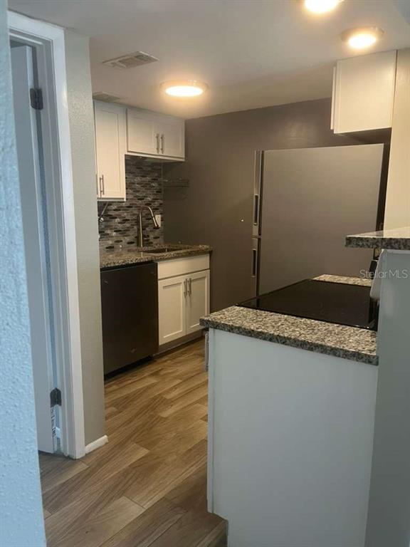 A kitchen features white cabinets, granite countertops, a dark dishwasher, and wood-look flooring — 131 WATER FRONT WAY UNIT 220, ALTAMONTE SPRINGS, FL