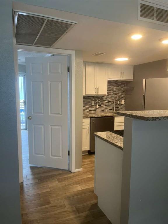 A kitchen with white cabinets and granite countertops is visible from a wood-floored hallway — 131 WATER FRONT WAY UNIT 220, ALTAMONTE SPRINGS, FL
