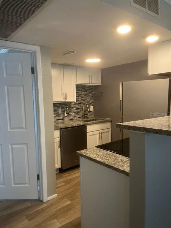 A kitchen features white cabinets, granite countertops, a stainless steel dishwasher, and wood-look flooring — 131 WATER FRONT WAY UNIT 220, ALTAMONTE SPRINGS, FL