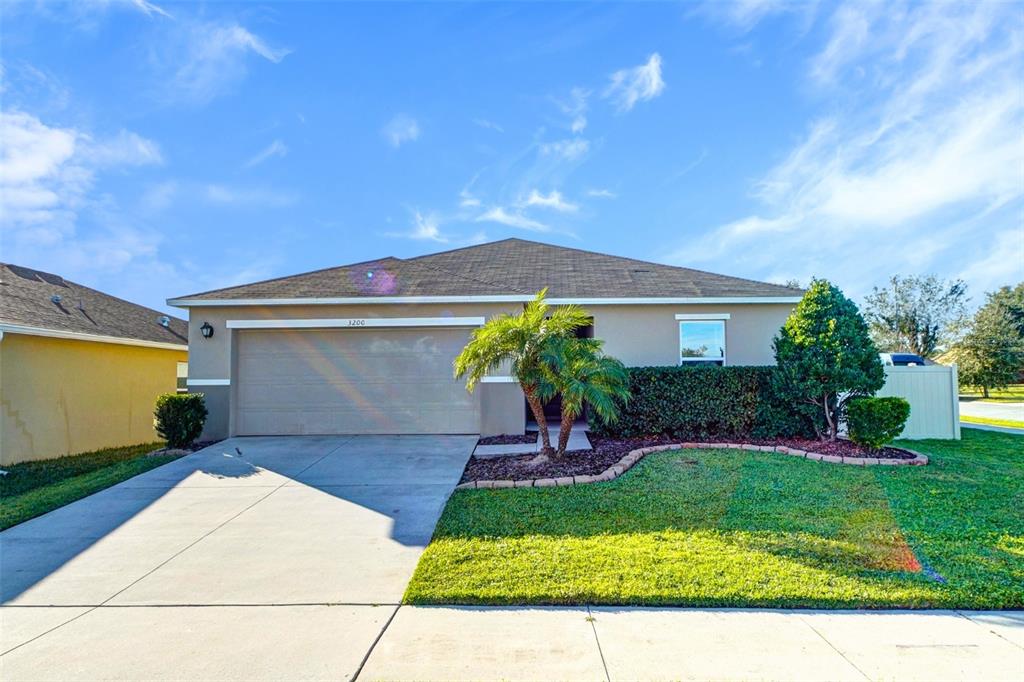 A single-story suburban house features a two-car garage, a palm tree, and a manicured lawn — 3200 CASA DEL REY AVENUE, KISSIMMEE, FL