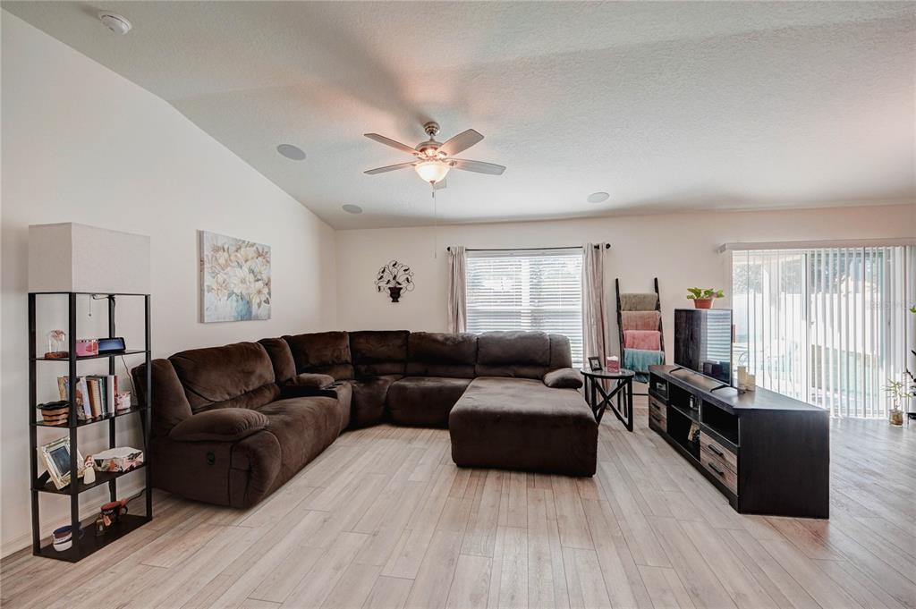 A living room features a large brown sectional sofa, wood-look flooring, and a ceiling fan — 3200 CASA DEL REY AVENUE, KISSIMMEE, FL