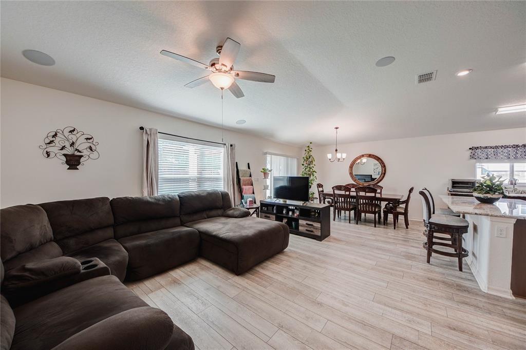 An open-concept living and dining area features a large sectional sofa and wood-look flooring — 3200 CASA DEL REY AVENUE, KISSIMMEE, FL