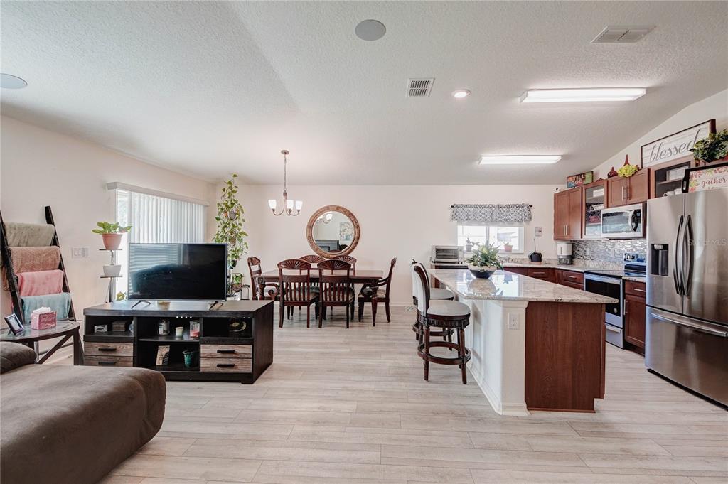 An open-concept kitchen, dining area, and living room featuring wood-look flooring and granite countertops — 3200 CASA DEL REY AVENUE, KISSIMMEE, FL