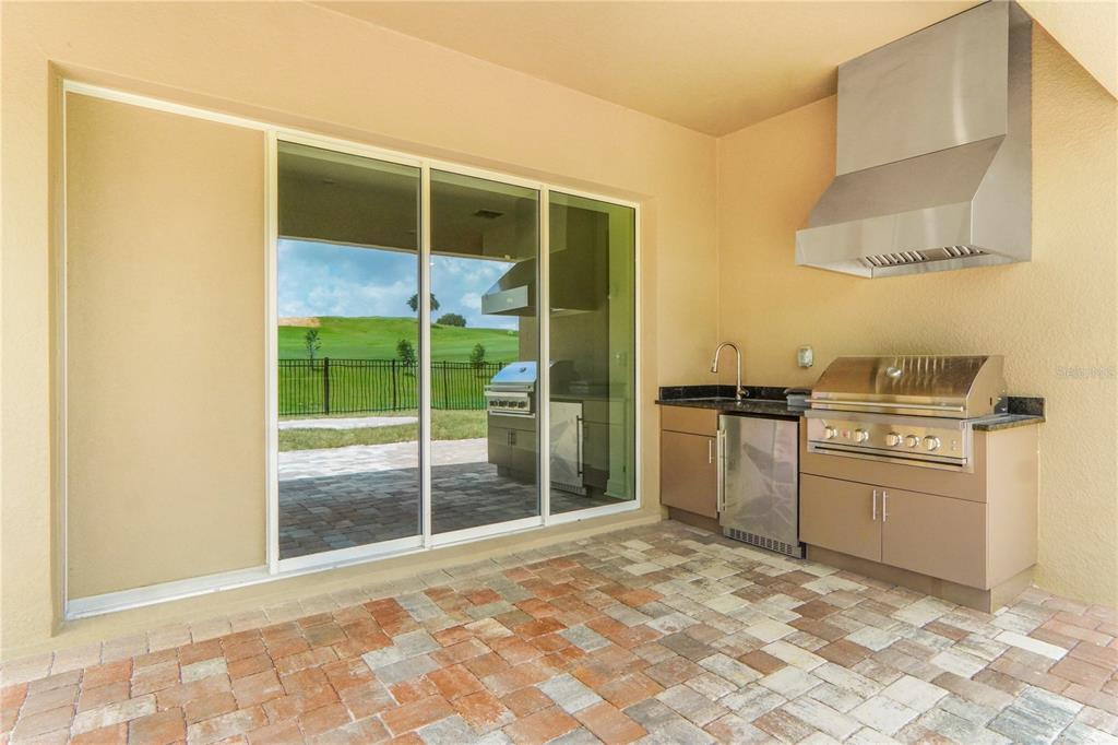 An outdoor kitchen with a grill, sink, and stainless steel hood sits on a paved patio — 16120 VOLTERRA POINT, MONTVERDE, FL
