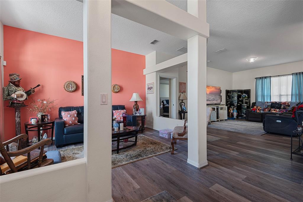 A living room with coral walls, dark wood-look flooring, and white structural support columns — 16 WHITE HAVEN LANE, PALM COAST, FL