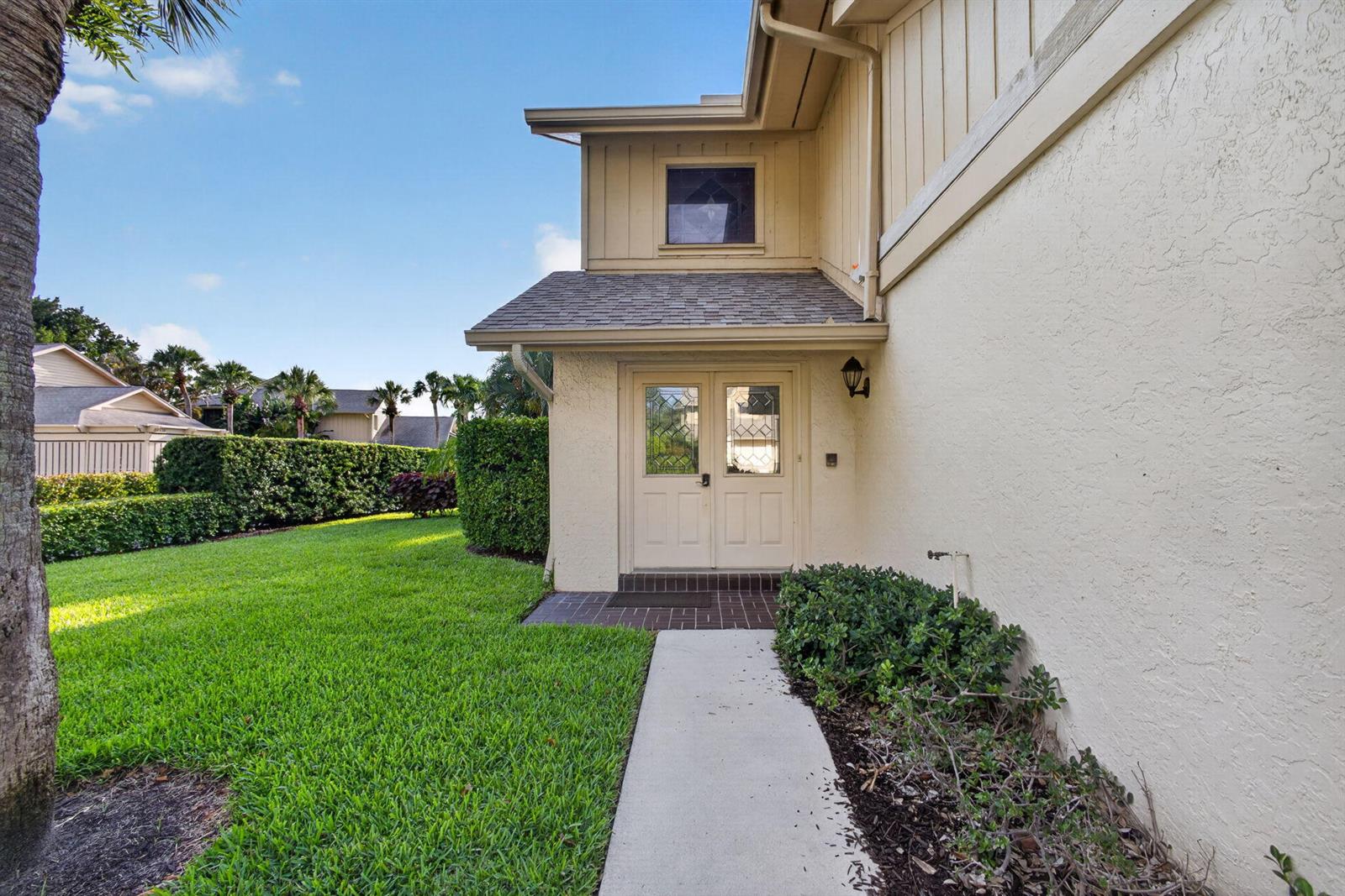A concrete walkway leads to the double front doors of a two-story tan house — 17137 Waterbend Drive # 204, Jupiter FL 33477, JUPITER, FL