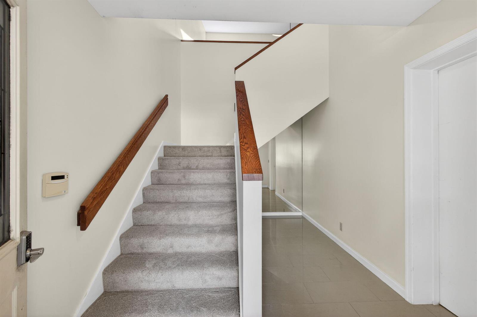 A carpeted staircase with a wooden handrail leads to an upper level in a foyer — 17137 Waterbend Drive # 204, Jupiter FL 33477, JUPITER, FL