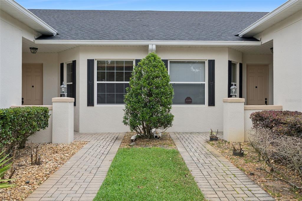 The exterior of a duplex features two tan doors, brick walkways, and a central shrub — 1005 GREEN GATE BOULEVARD, GROVELAND, FL