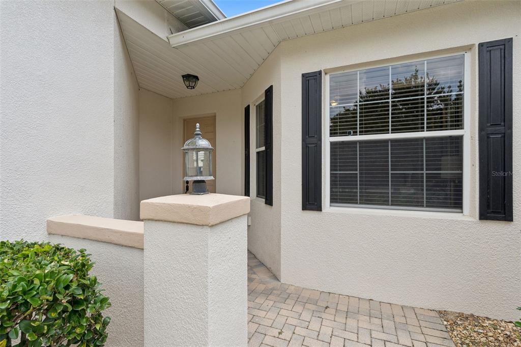 A paved walkway leads to the recessed front entrance of a stucco home with shutters — 1005 GREEN GATE BOULEVARD, GROVELAND, FL