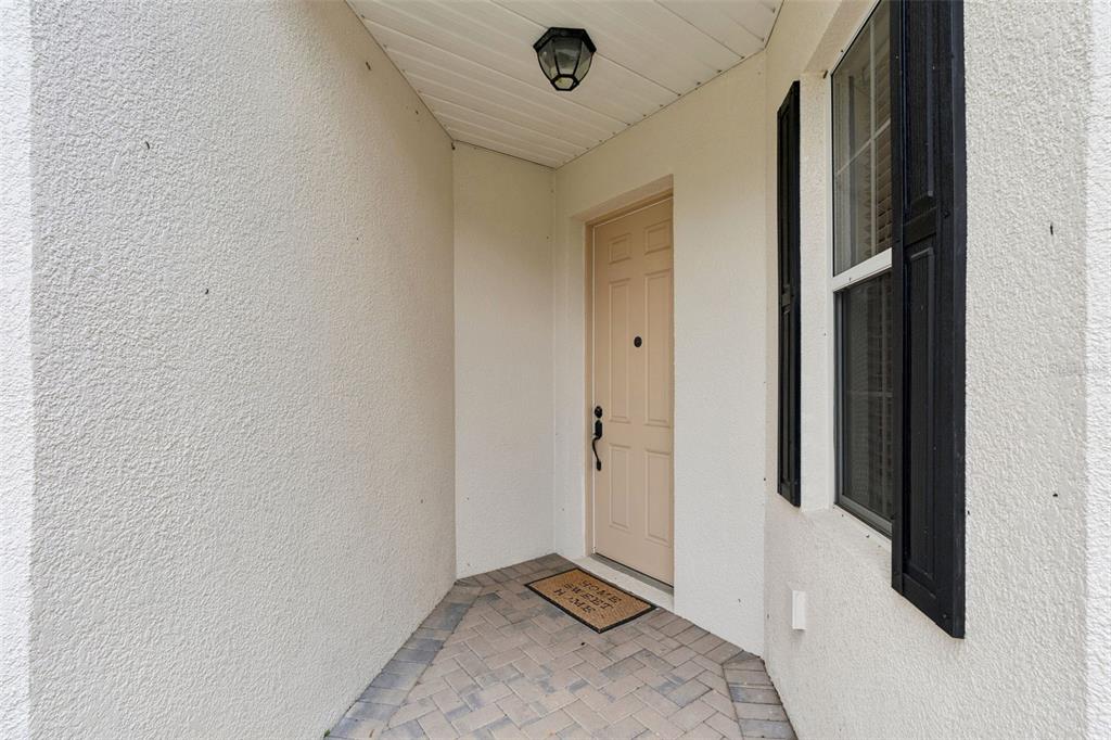 A covered entryway features a light-colored door, a brick paver floor, and a window — 1005 GREEN GATE BOULEVARD, GROVELAND, FL