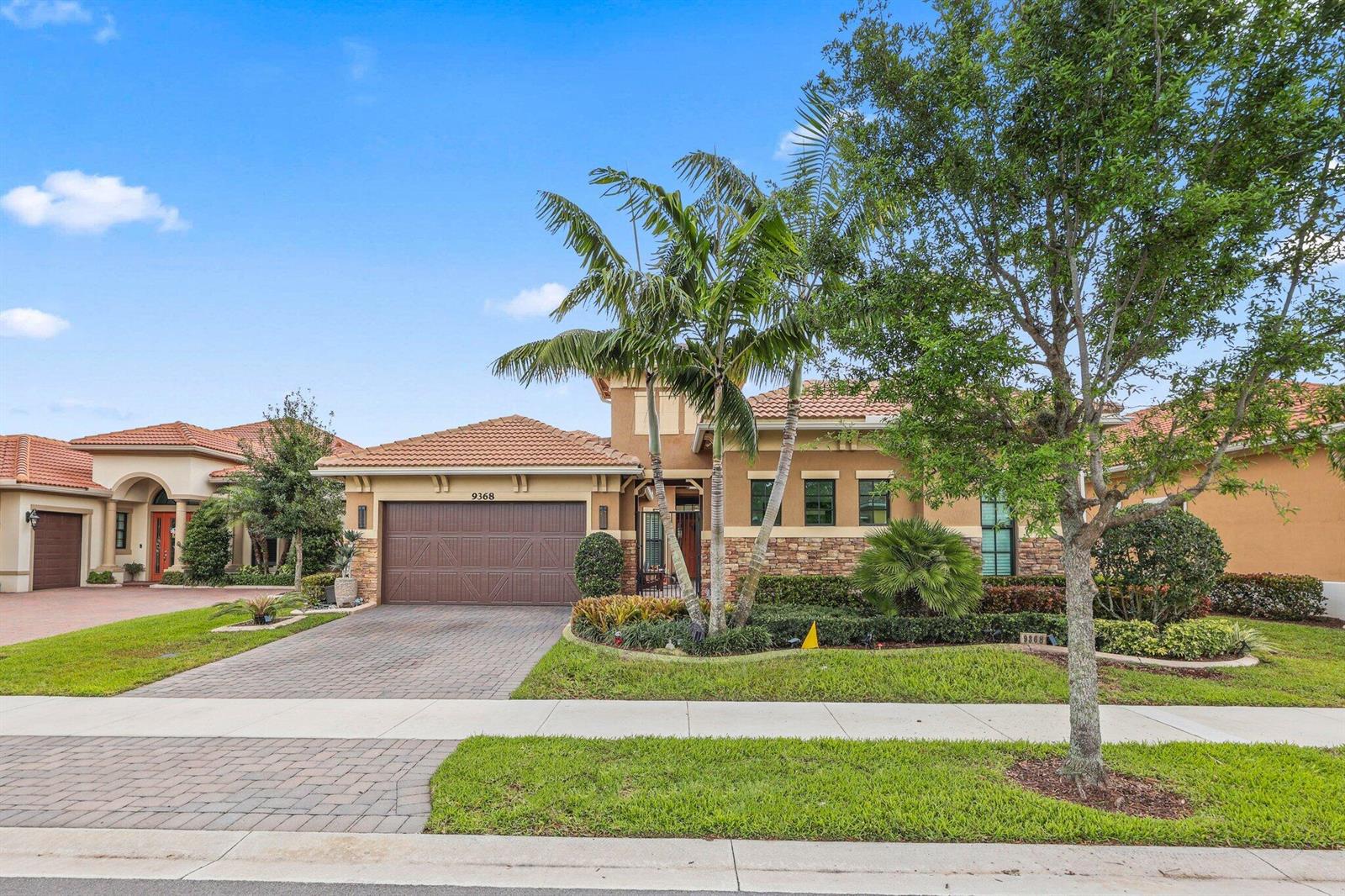 A single-story suburban house with a brown garage, tile roof, and palm trees in front — 9368 Cantal Circle E, Parkland FL 33076, PARKLAND, FL