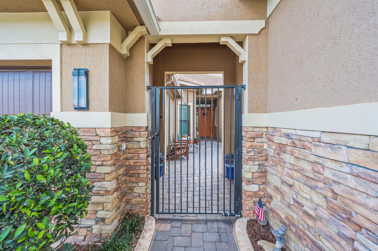 A metal gate leads to a paved courtyard entrance with stone siding and stucco walls — 9368 Cantal Circle E, Parkland FL 33076, PARKLAND, FL