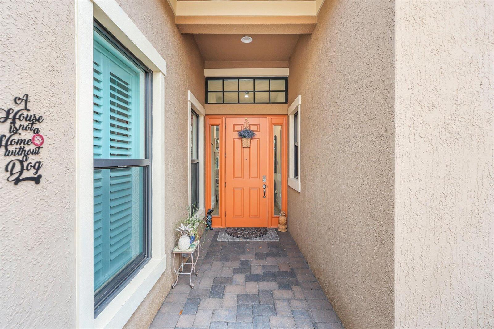 A covered entryway features a bright orange front door, tiled flooring, and teal window shutters — 9368 Cantal Circle E, Parkland FL 33076, PARKLAND, FL