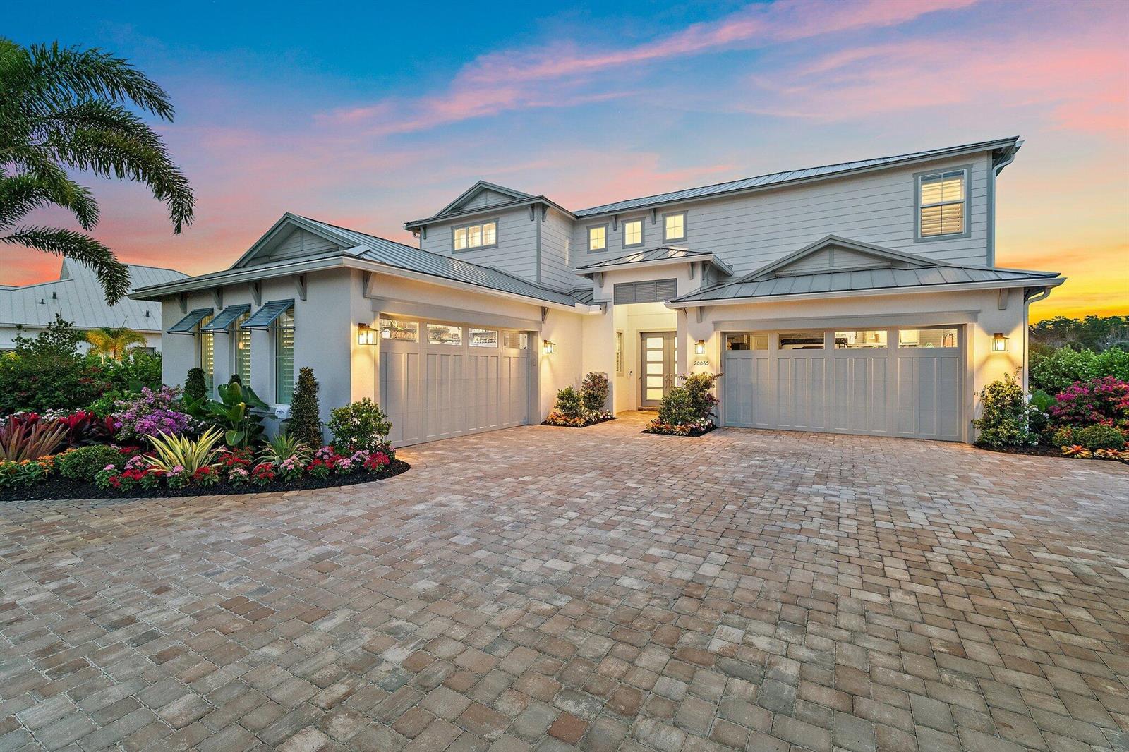 A two-story house with a paved driveway, two garages, and colorful landscaping at sunset — 20065 SE Bridgewater Drive, Jupiter FL 33458, JUPITER, FL