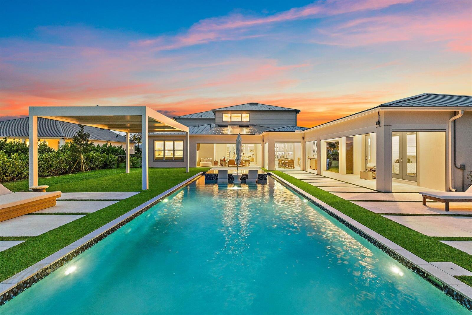 A modern house exterior features a long swimming pool, a pergola, and a landscaped patio — 20065 SE Bridgewater Drive, Jupiter FL 33458, JUPITER, FL