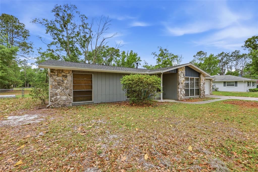 A single-story house with gray vertical siding and stone accents sits on a grassy lot — 2921 NW 54TH AVENUE, GAINESVILLE, FL