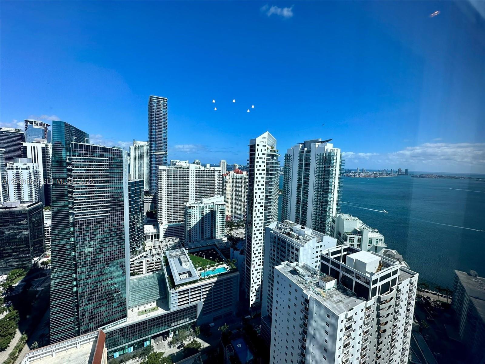 An elevated view of a dense city skyline featuring high-rise buildings and a large bay — 1425 Brickell Ave # 42E, Miami FL 33131, MIAMI, FL
