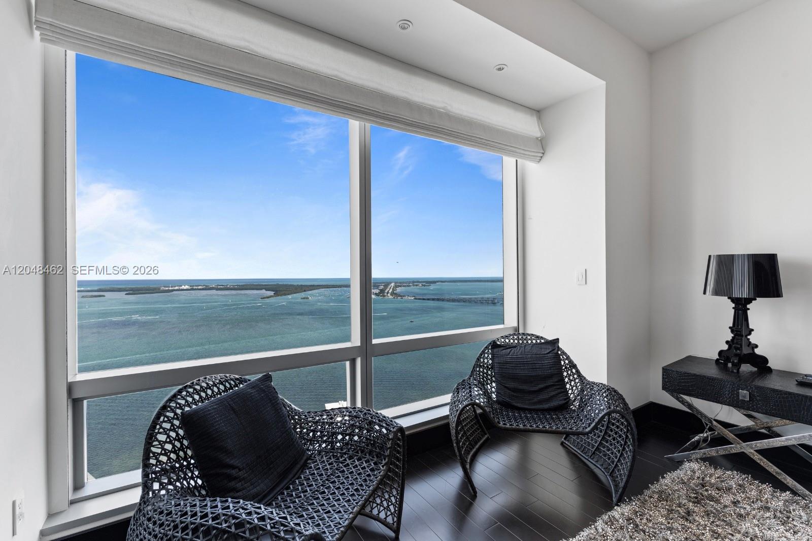 A modern room features two dark woven chairs, a black console table, and floor-to-ceiling ocean views — 1425 Brickell Ave # 42E, Miami FL 33131, MIAMI, FL