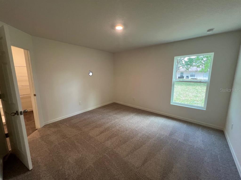 A bedroom with beige carpet, white walls, a window, and an open closet door — 76 RALEIGH DRIVE, PALM COAST, FL