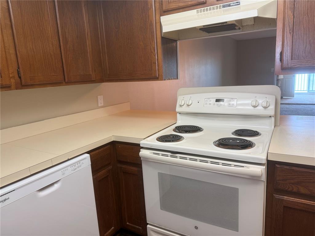 A kitchen with wood cabinets, white appliances, and beige countertops — 607 COUNTRY LANE NE UNIT 607, WINTER HAVEN, FL