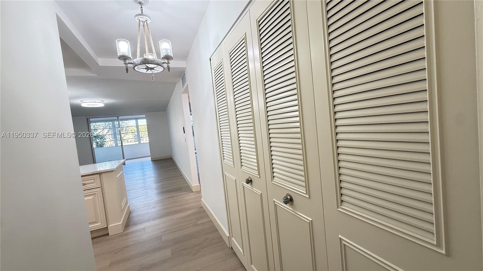 A hallway with louvered closet doors leads to an open living area with wood flooring — 370 NW 76th Ave # 204, Margate FL 33063, MARGATE, FL