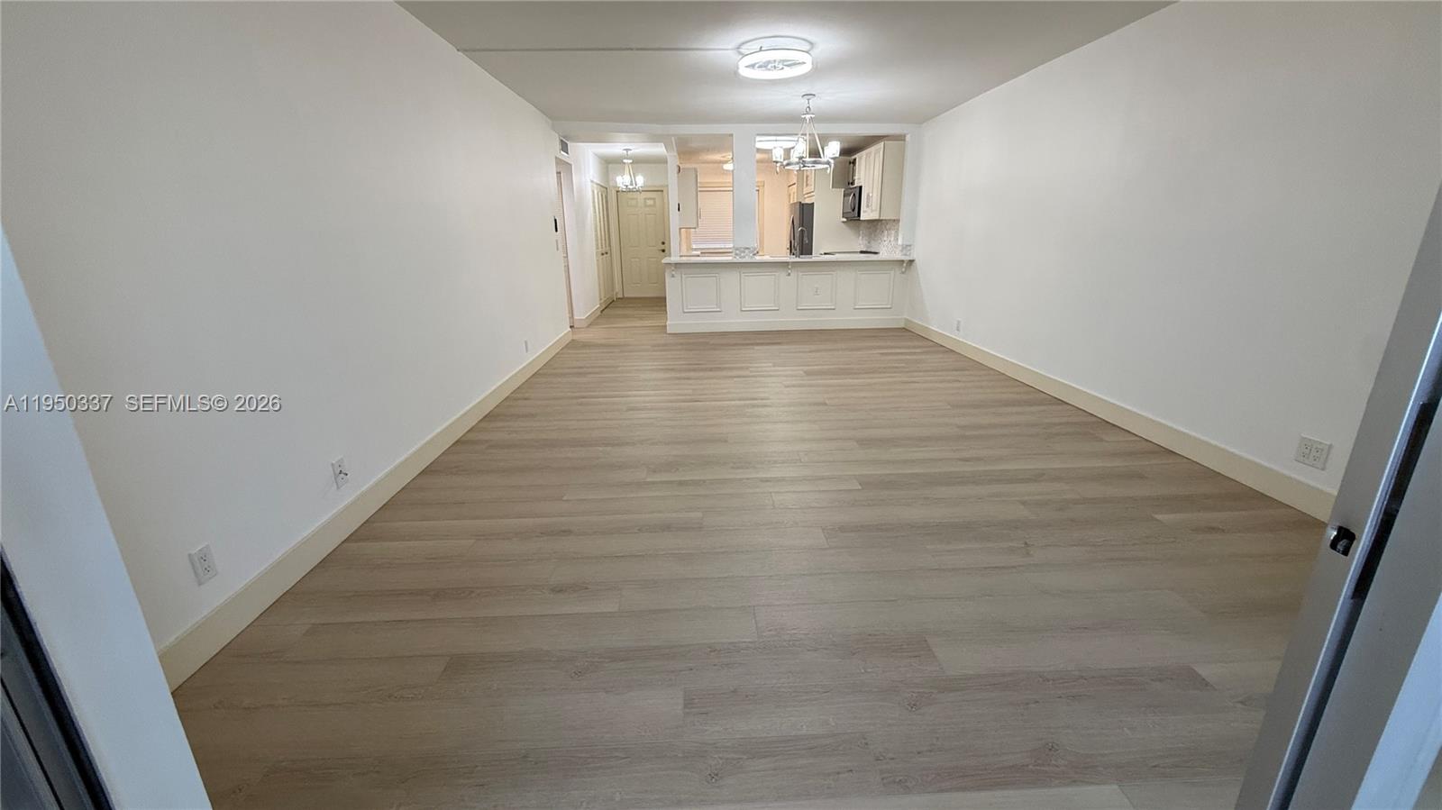 An empty living area with light wood-look flooring leads to an open kitchen with a counter — 370 NW 76th Ave # 204, Margate FL 33063, MARGATE, FL