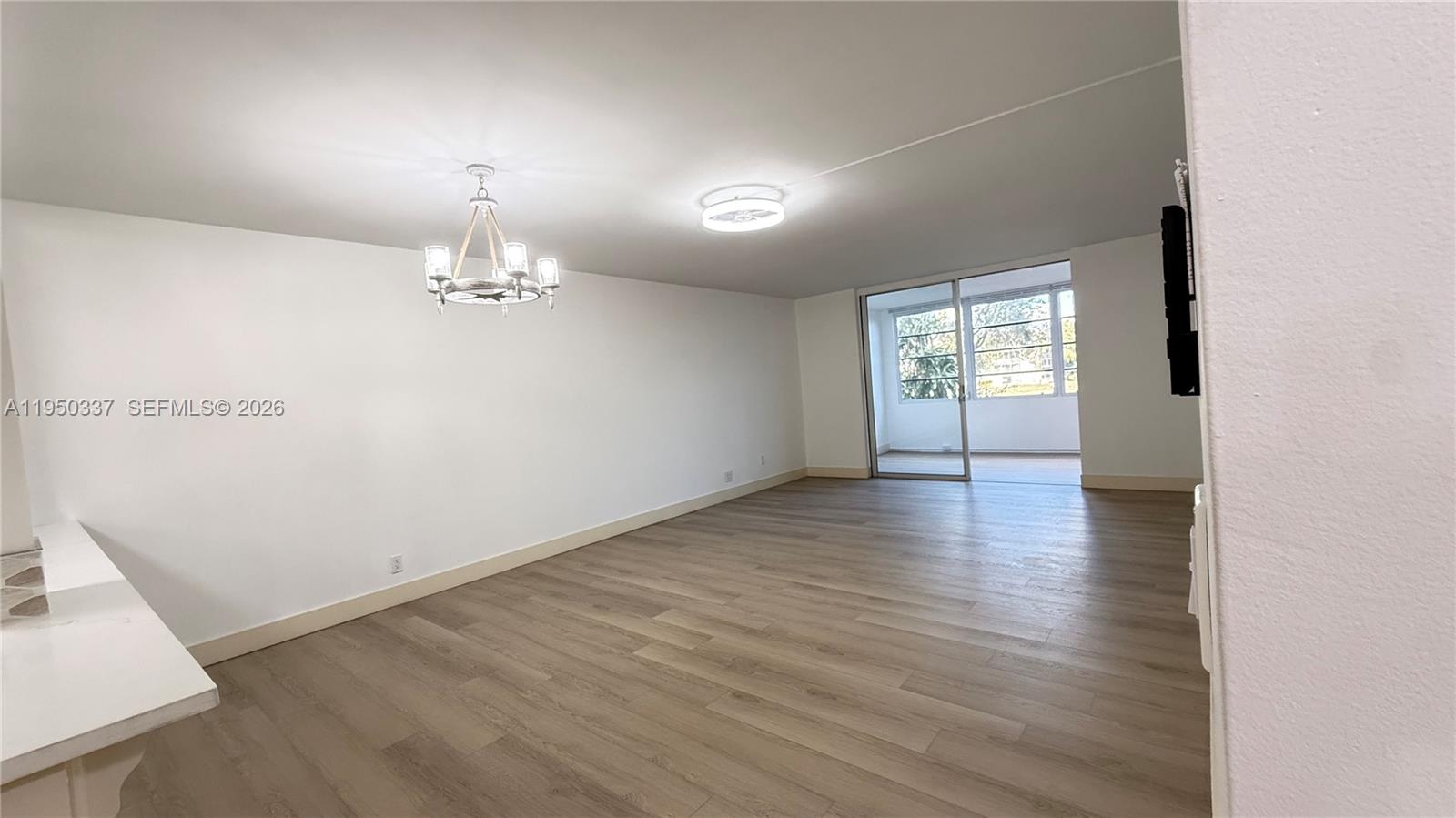 An empty living room features light wood-look flooring, a chandelier, and a sliding glass door — 370 NW 76th Ave # 204, Margate FL 33063, MARGATE, FL
