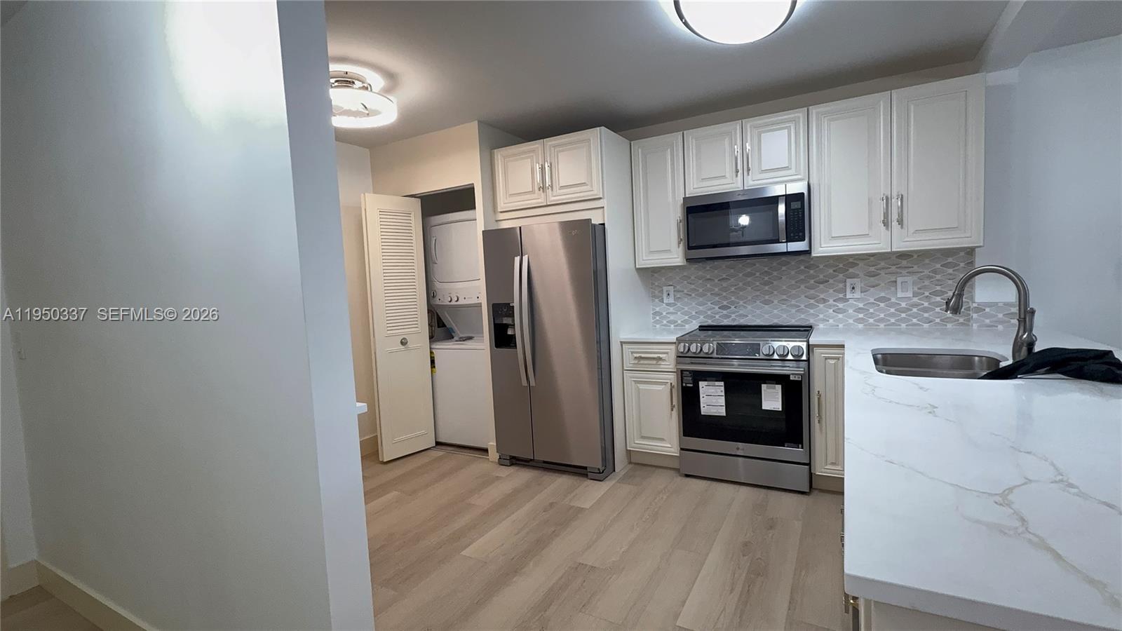 A kitchen features white cabinets, stainless steel appliances, a tiled backsplash, and light wood flooring — 370 NW 76th Ave # 204, Margate FL 33063, MARGATE, FL