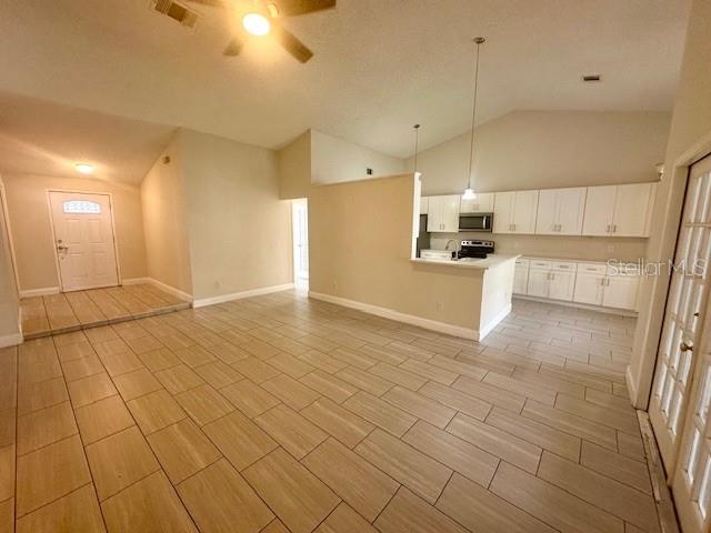 An open-concept living area features light-colored tile flooring, a kitchen with white cabinets, and vaulted ceilings — 12686 NEWFIELD DRIVE, ORLANDO, FL
